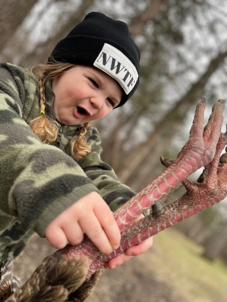 A young girld holds a harvested wild turkey by the legs. 