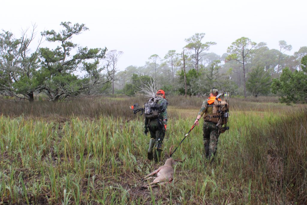 Hunters carry a harvested buck to their boat.