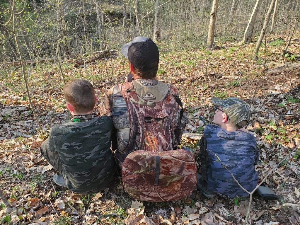 a hunter sit with young hunters on each side of him.