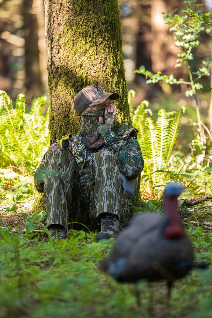 A hunter calls a turkey as they lean up against a tree.