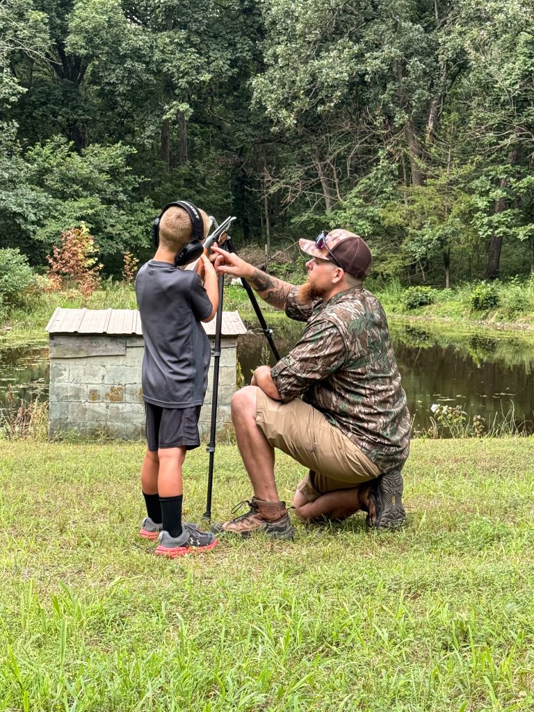 Youth practices shooting shotgun over pond.