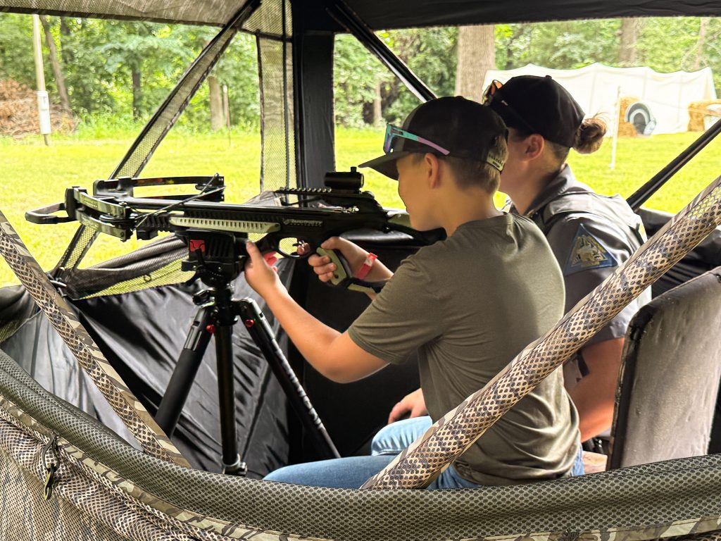 Youth shoots a crossbow in a blind with a mentor.