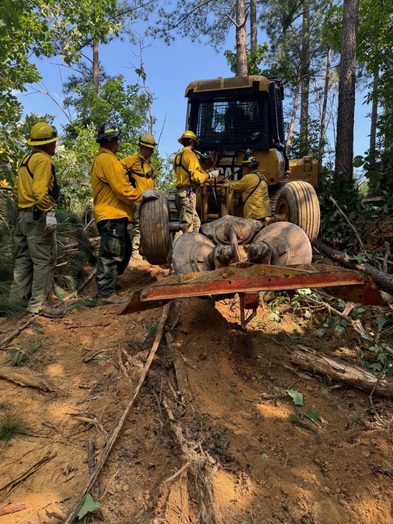 Wildland firefighters attach an implement t oa dozer.