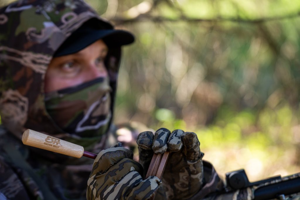 Hunter leaning up against a tree uses a pot call.